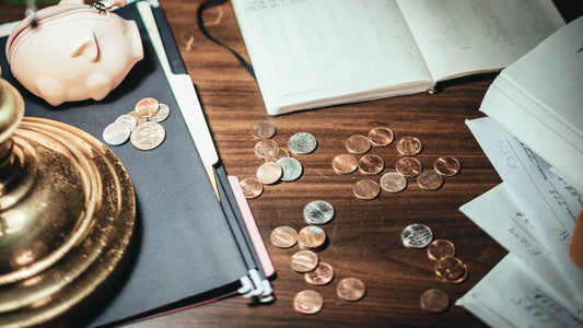 Coins spread across a desk next to a piggy coin purse and an open notebook