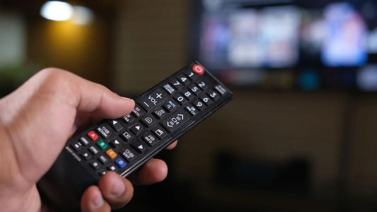 Hand holding a TV remote control in a dimly lit living room