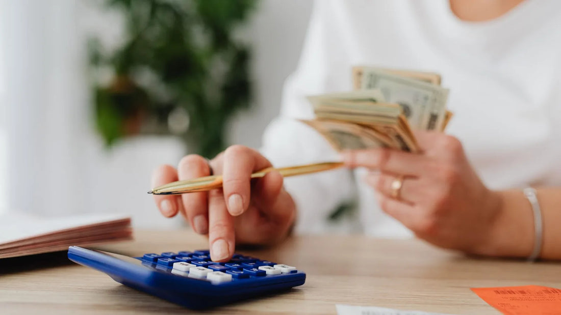 Hands using a calculator while counting cash on a desk, reviewing household spending during a statement audit