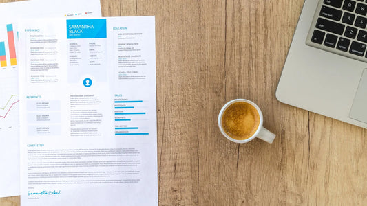 Printed resume, a cup of coffee and a laptop on a wooden desk