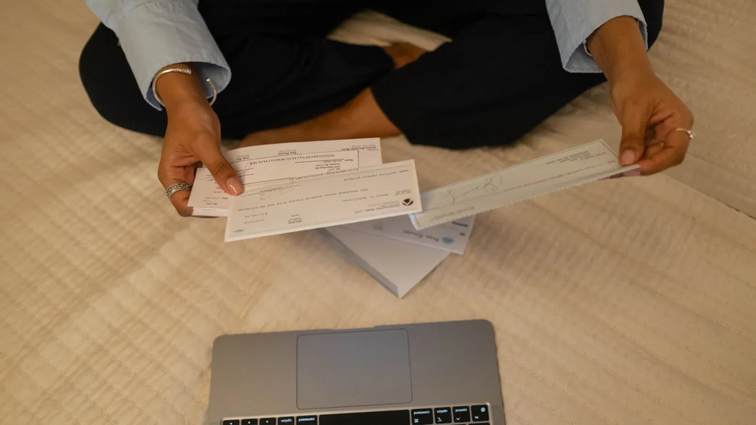 Person holding paychecks while sitting beside a laptop