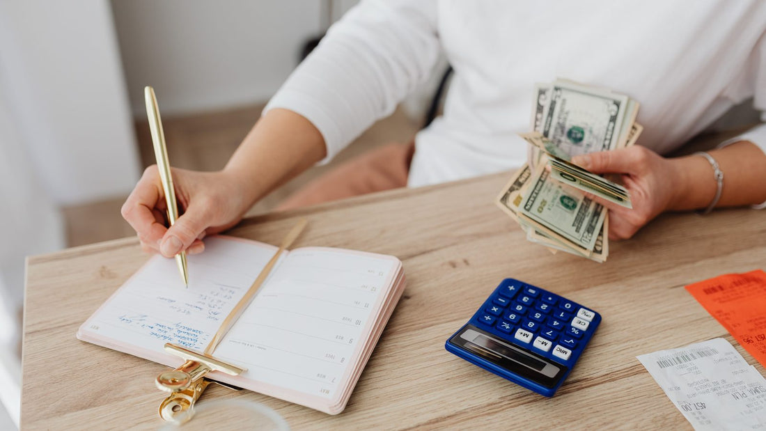 Person counting cash and writing in a planner next to a calculator and receipts, budgeting for beginners