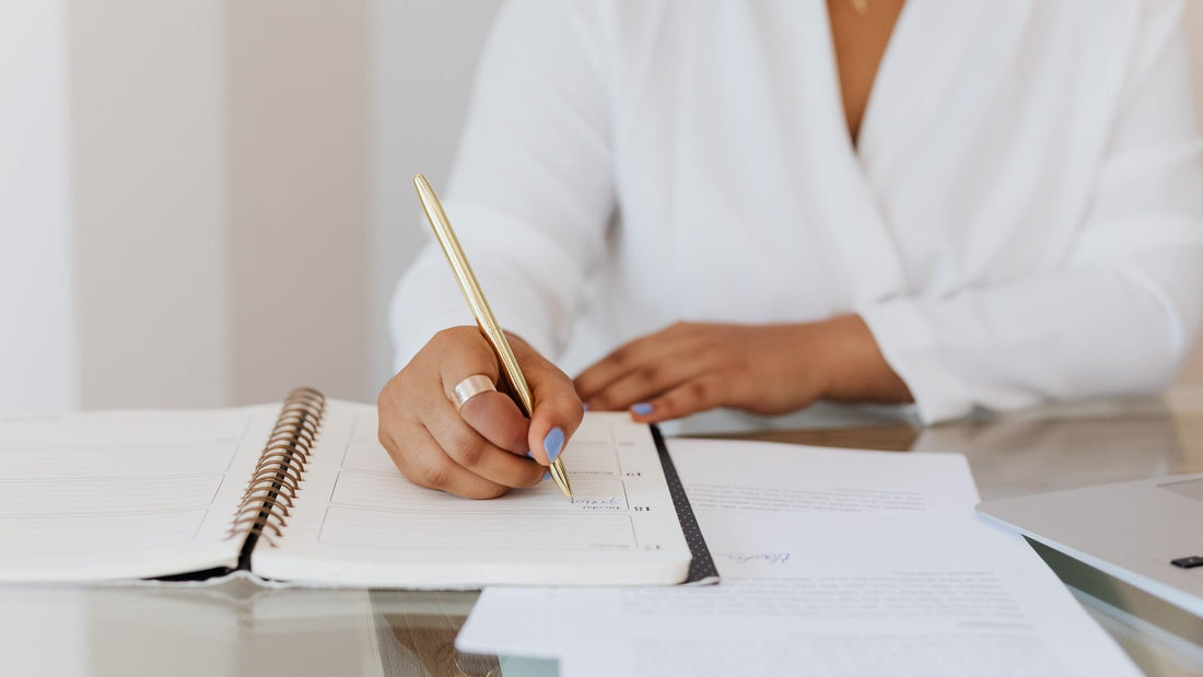 Person writing in a paper planner with a gold pen instead of using a spreadsheet
