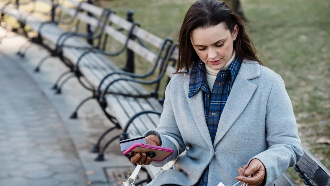 Woman on a park bench holding her phone and a payment card while looking into a shopping bag