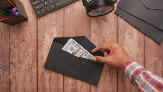 Hand placing a dollar bill into a black envelope on a wooden desk