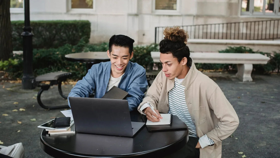 Two students working on a laptop at an outdoor campus table