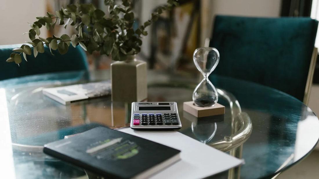 Hourglass beside a calculator and notebook on a glass table