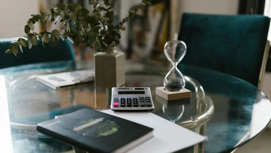 Hourglass beside a calculator and notebook on a glass table