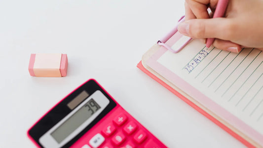 Hand writing a list on a clipboard next to a pink calculator