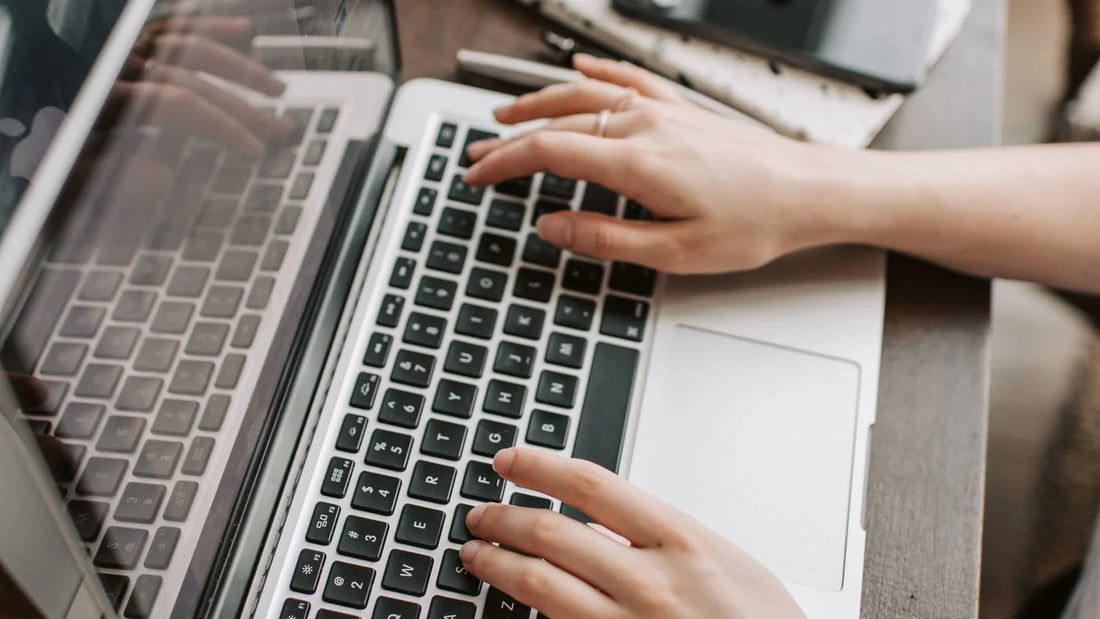 Close-up of hands typing on a laptop keyboard at a home desk