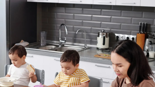 Mother working on a laptop at the kitchen table while her children eat breakfast