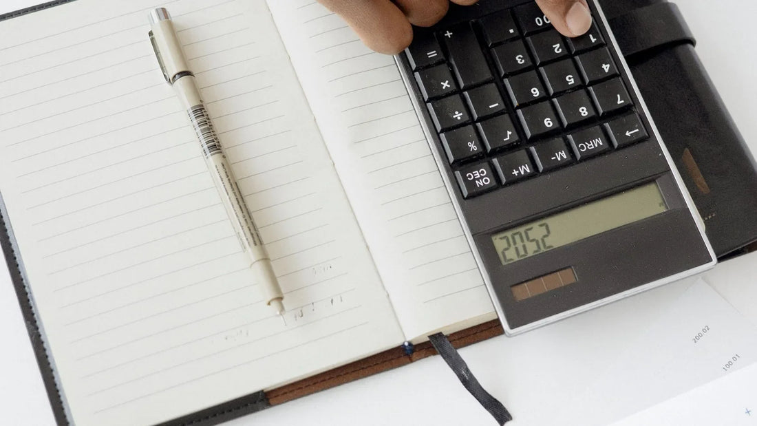 Hand on a calculator beside an open notebook and pen