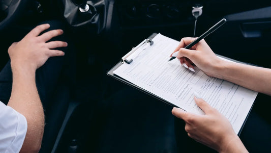 Person filling out an insurance form on a clipboard while sitting in the front seat of a car