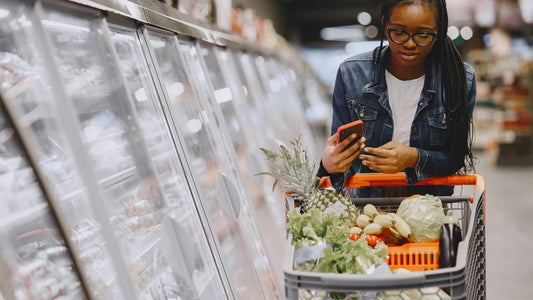Woman pushing a shopping cart through a grocery store while checking her phone