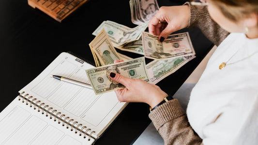 Person counting cash next to an open budget planner and pen