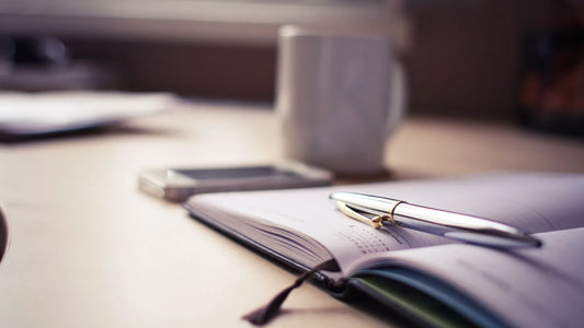 Open planner with a pen beside a coffee mug on a desk