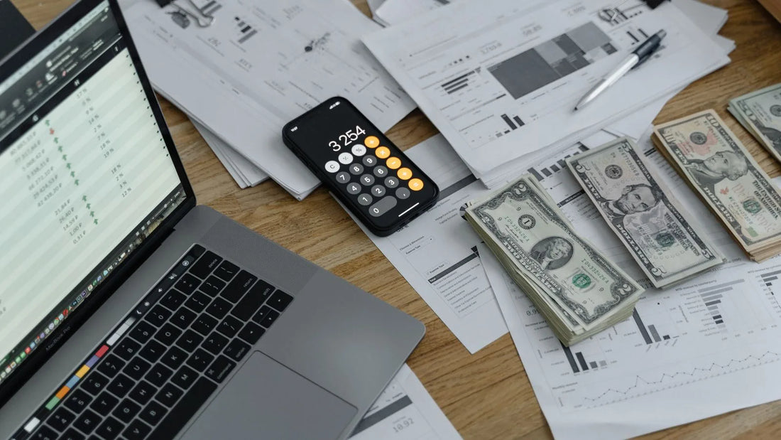 Overhead view of a calculator, cash, financial documents, and a laptop on a wooden desk