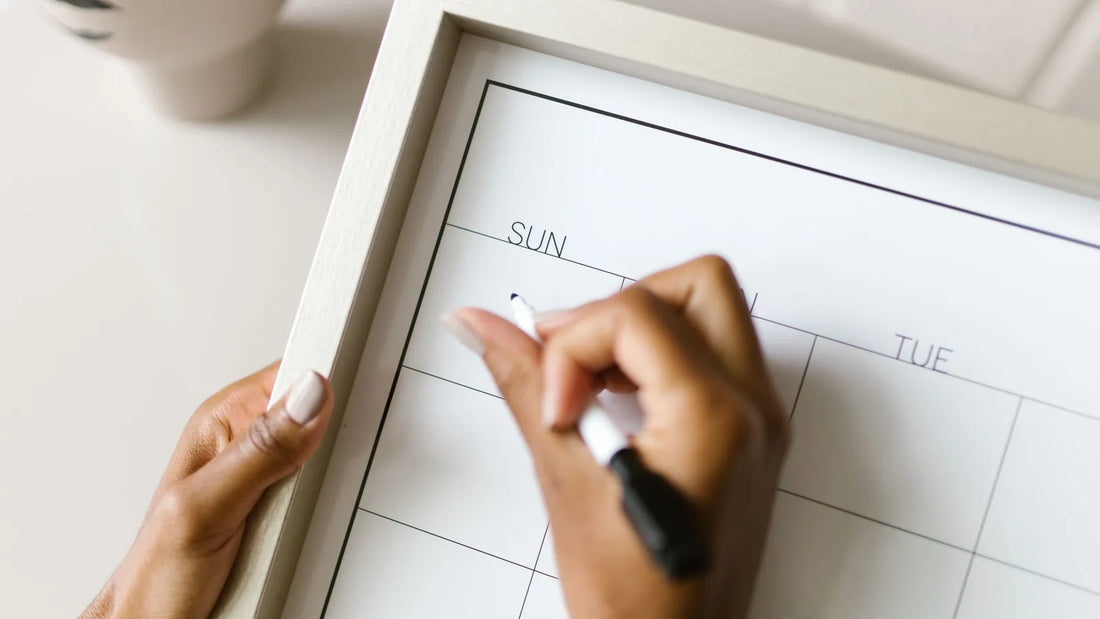 Hands writing on a blank monthly wall calendar with a marker while planning the month ahead