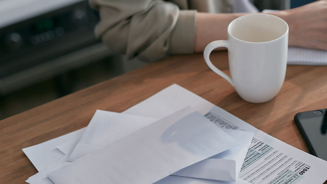 Stack of envelopes and a tax form next to a coffee mug on a wooden desk, representing organizing bills