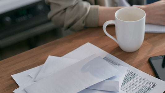 Stack of envelopes and a tax form next to a coffee mug on a wooden desk, representing organizing bills