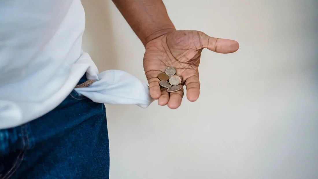 Person holding a few coins in an open palm beside an empty pocket