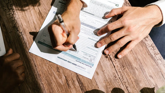 Person filling out a loan form with a pen on a wooden table