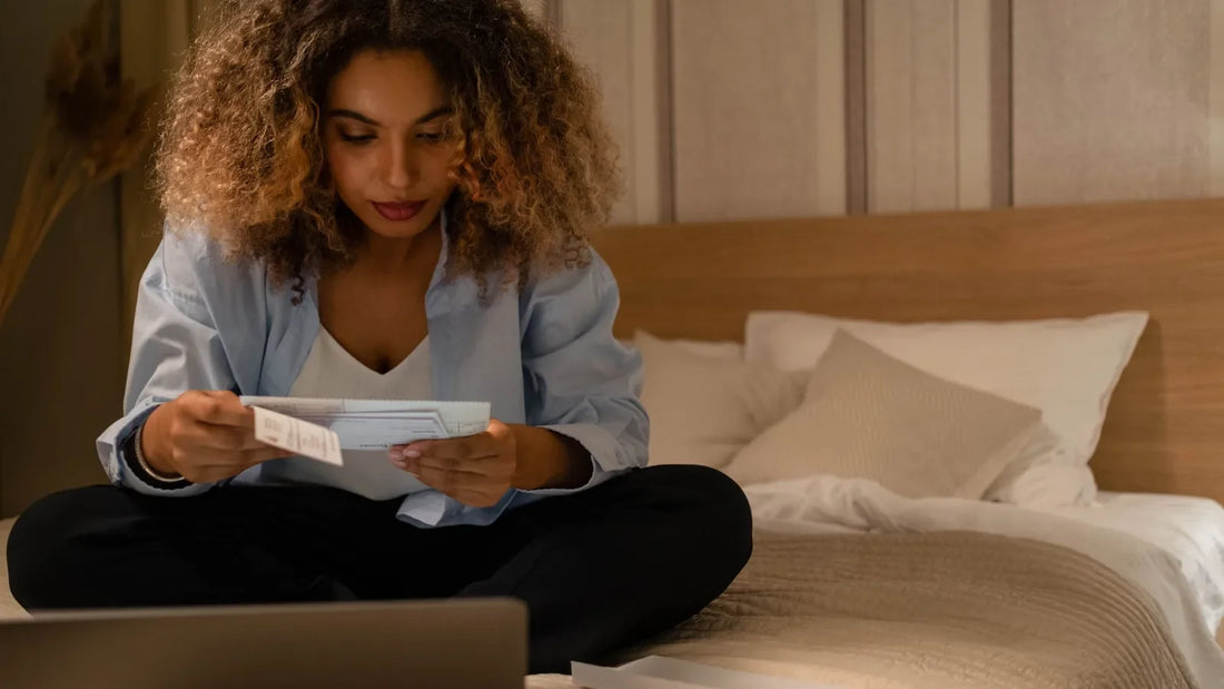 Woman sitting cross-legged on her bed reading a printed pay statement at home