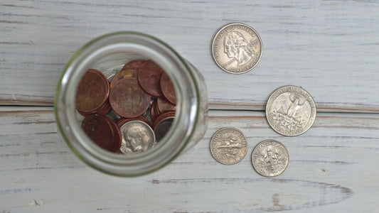 Overhead view of a jar filled with coins on a wooden table, representing a savings goal