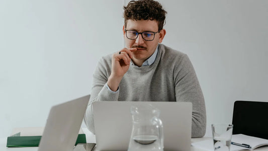 Man in glasses thinking while working on a laptop