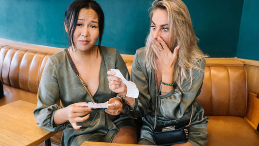 Two friends in a restaurant booth looking surprised as they read the check after a meal out