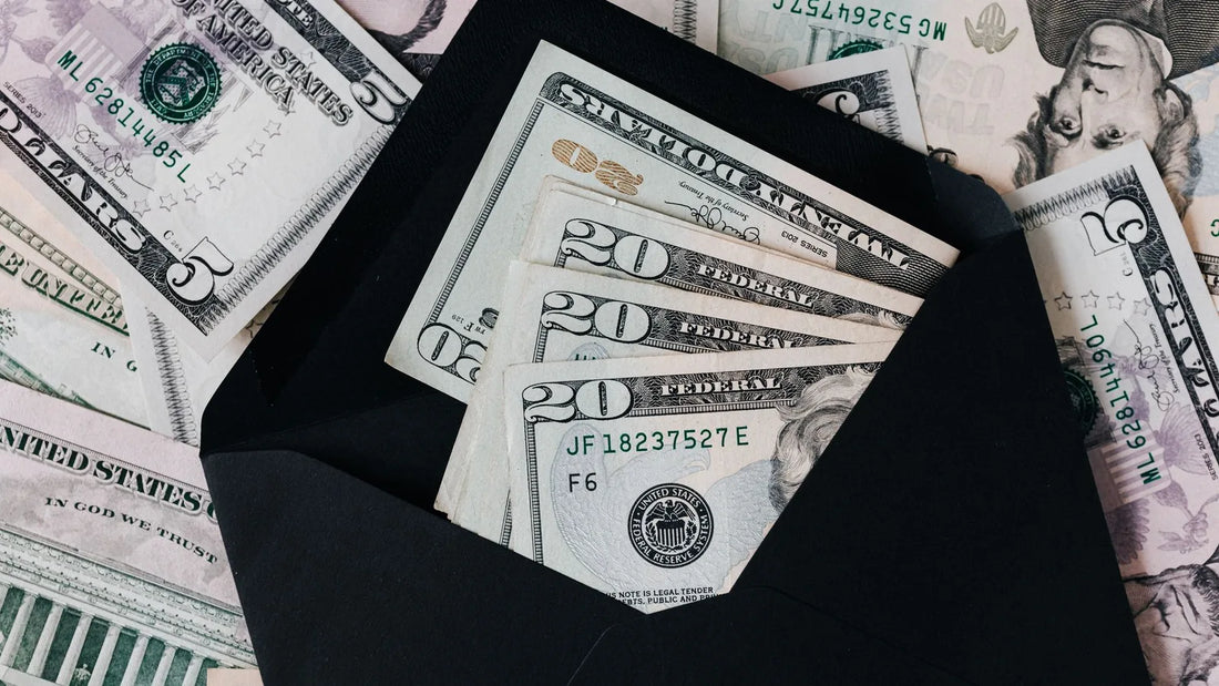 Cash tucked inside an open envelope on top of a spread of dollar bills, representing money set aside for a sinking fund