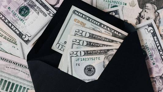 Cash tucked inside an open envelope on top of a spread of dollar bills, representing money set aside for a sinking fund