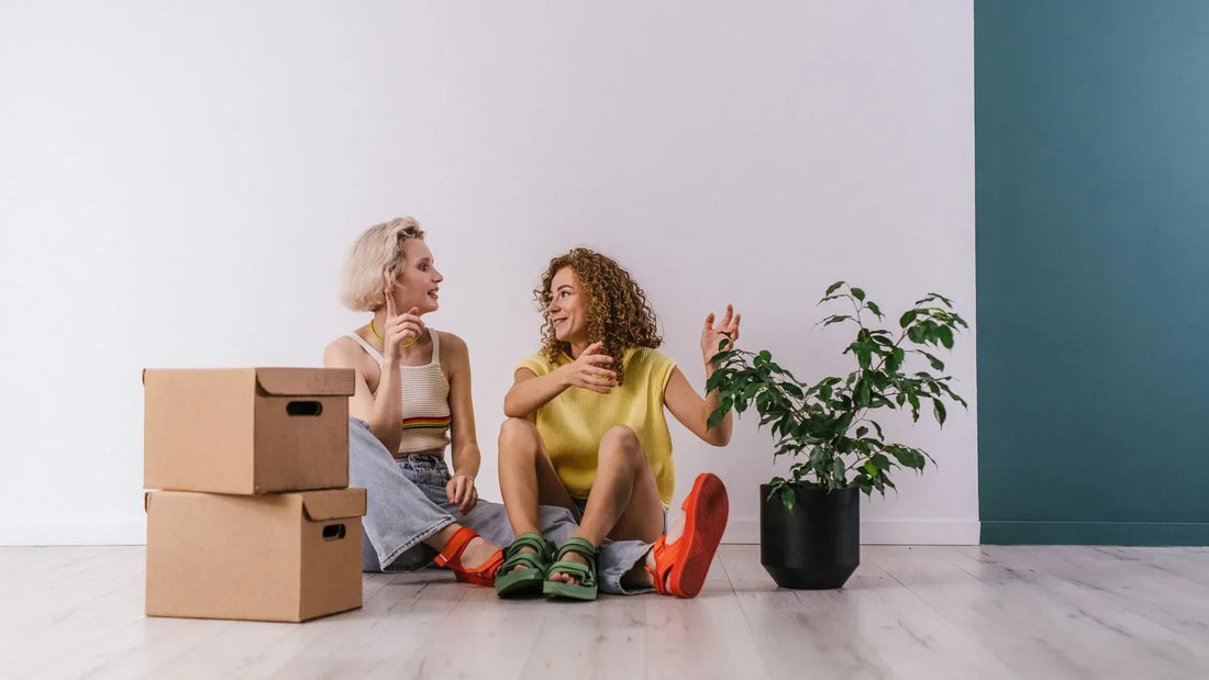 Two women chatting on the floor of a new apartment beside moving boxes