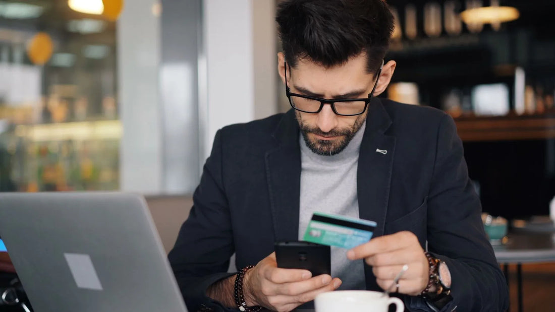 Man in a café holding a credit card and phone while making an online purchase