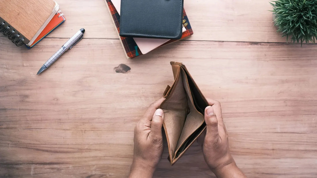 Hands holding an open, empty wallet over a wooden desk