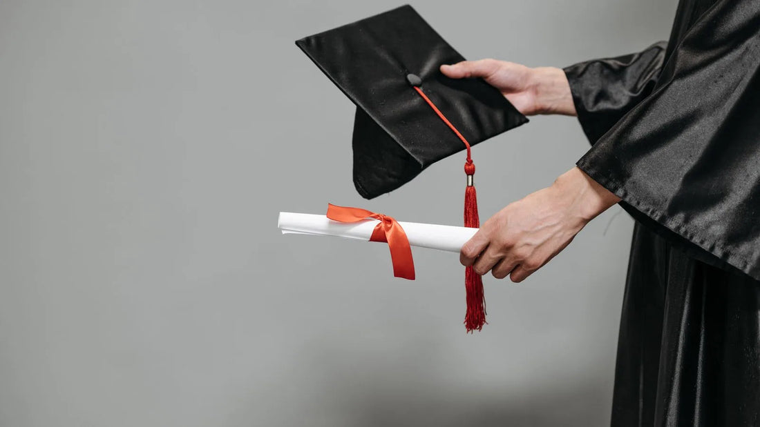 Graduate holding a cap and a diploma tied with a red ribbon