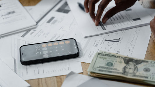 Close-up of a phone calculator, cash, and financial documents on a desk while reviewing spending