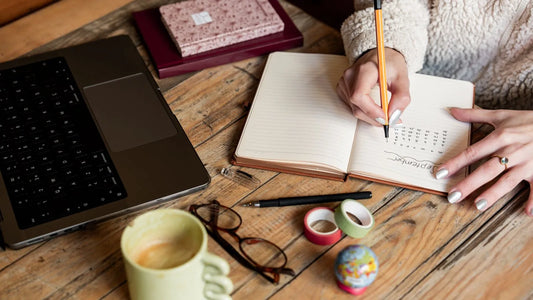 Woman writing in a notebook beside a laptop and a cup of coffee during a weekly money check-in