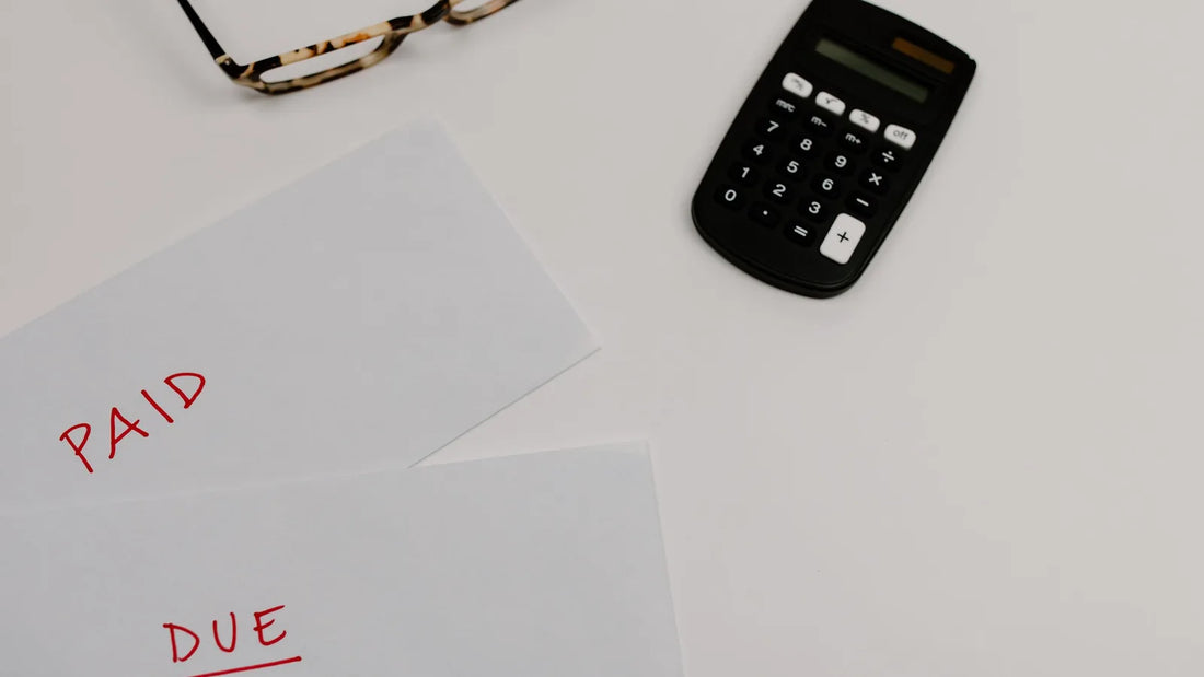 Papers marked paid and due next to a calculator and glasses