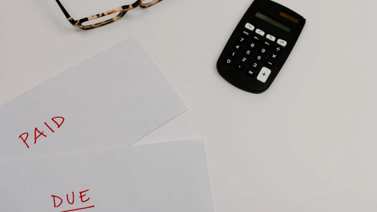 Papers marked paid and due next to a calculator and glasses