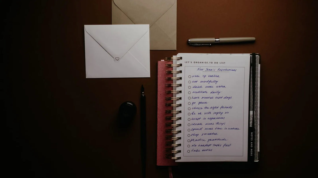Notebook with a handwritten checklist, pens and envelopes on a dark desk