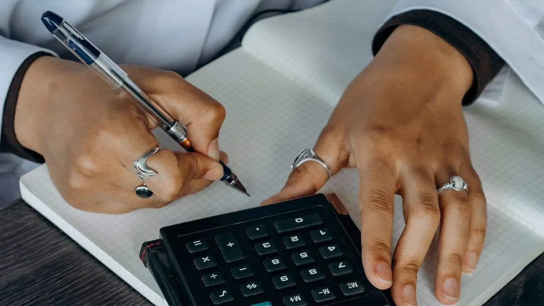 Hands writing figures in a notebook beside a calculator